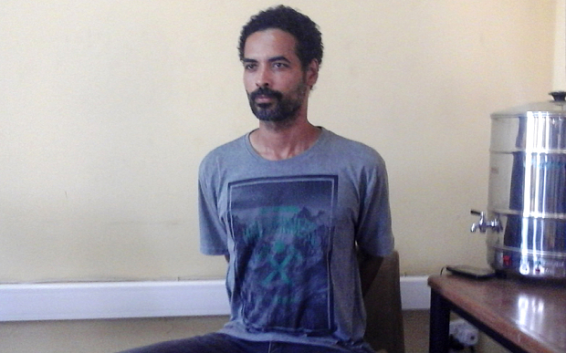 Arthur Simpson-Kent handcuffed behind  at he headquarters of Ghana's Criminal Investigations Department(CID) 1.48 pm, Sunday,  January, 10, 2016.

From: "Justice Lee Adoboe" 
Unshaven  with bushy hear. Spotting a grey T-shirt with the inscription,  "Wilderness" under which is the image of crossed hammers.

He is also in a pair of grey jeans trousers with leather dark leather sandals.