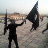 A fighter of the Islamic State of Iraq and the Levant (ISIL) holds an ISIL flag and a weapon on a street in the city of Mosul, June 23, 2014. REUTERS/Stringer/Files