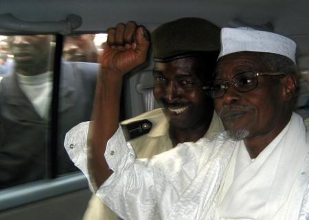 Former Chad President Hissene Habre (R) raises his fist in the air as he leaves a court in Dakar escorted by a Senegalese policeman November 25, 2005.  REUTERS/Aliou Mbaye