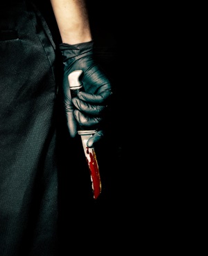 Black gloved hand holding a bloody knife.