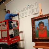 A man hangs a sign as artist Frida Kahlo's painting 'Nina Con Collar' sits on an easel at Sotheby's auction house in New York U.S., November 14, 2016. REUTERS/Shannon Stapleton