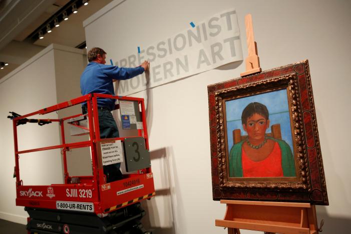 A man hangs a sign as artist Frida Kahlo's painting 'Nina Con Collar' sits on an easel at Sotheby's auction house in New York U.S., November 14, 2016. REUTERS/Shannon Stapleton