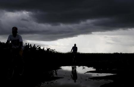 Storm clouds hover as cyclists pass a field of maize after late rains near Malawi's capital Lilongwe, February 1, 2016.   REUTERS/Mike Hutchings