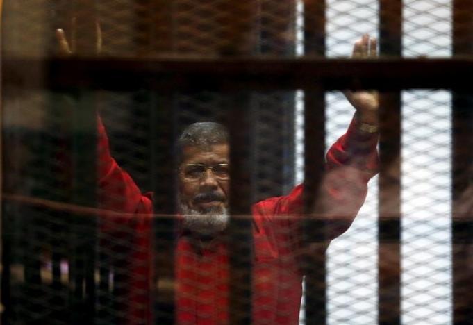 Former Egyptian President Mohamed Mursi greets his lawyers and people from behind bars at a court wearing the red uniform of a prisoner sentenced to death, during his court appearance with Muslim Brotherhood members on the outskirts of Cairo, Egypt, June 21, 2015. REUTERS/Amr Abdallah Dalsh/File Photo