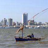 Traditional fishing boats sail as Mozambique's tuna fleet sits in dock beneath Maputo's skyline, in this picture taken August 15, 2015. Mozambique, one of the world's poorest countries, discovered the reserves off its coast between 2010-2013, offering an opportunity to transform the former Portuguese colony which was ravaged by a 16-year civil war that ended in 1992. Recent signs of reckless government spending and an uptick in political violence have raised concerns that Mozambique could be the latest African country to suffer the resource "curse," in which an influx of petro-dollars suffocates the rest of the economy, encourages corruption and stirs unrest.  Picture taken August 15, 2015.  REUTERS/Grant Lee Neuenburg - RTX1TA2Z