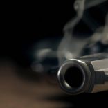 A gritty images of a smoking hand gun laying on the floor with narrow focus on the tip if the barrel