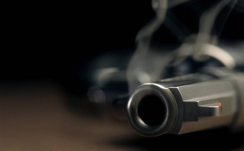 A gritty images of a smoking hand gun laying on the floor with narrow focus on the tip if the barrel