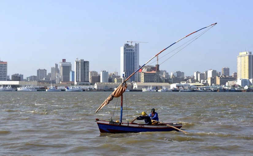 Traditional fishing boats sail as Mozambique's tuna fleet sits in dock beneath Maputo's skyline, in this picture taken August 15, 2015. Mozambique, one of the world's poorest countries, discovered the reserves off its coast between 2010-2013, offering an opportunity to transform the former Portuguese colony which was ravaged by a 16-year civil war that ended in 1992. Recent signs of reckless government spending and an uptick in political violence have raised concerns that Mozambique could be the latest African country to suffer the resource "curse," in which an influx of petro-dollars suffocates the rest of the economy, encourages corruption and stirs unrest.  Picture taken August 15, 2015.  REUTERS/Grant Lee Neuenburg - RTX1TA2Z