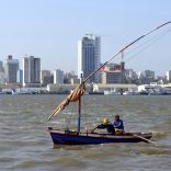 Traditional fishing boats sail as Mozambique's tuna fleet sits in dock beneath Maputo's skyline, in this picture taken August 15, 2015. Mozambique, one of the world's poorest countries, discovered the reserves off its coast between 2010-2013, offering an opportunity to transform the former Portuguese colony which was ravaged by a 16-year civil war that ended in 1992. Recent signs of reckless government spending and an uptick in political violence have raised concerns that Mozambique could be the latest African country to suffer the resource "curse," in which an influx of petro-dollars suffocates the rest of the economy, encourages corruption and stirs unrest.  Picture taken August 15, 2015.  REUTERS/Grant Lee Neuenburg - RTX1TA2Z