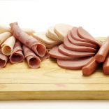 29027715 - a collection of cold meats, bologna, and vienna sausages on a wooden board on an isolated white studio background
